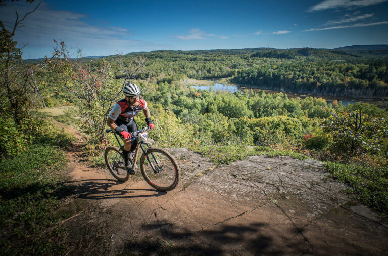 a grat shot of a bike rider on an exposed ledge overlooking the forest in the distance