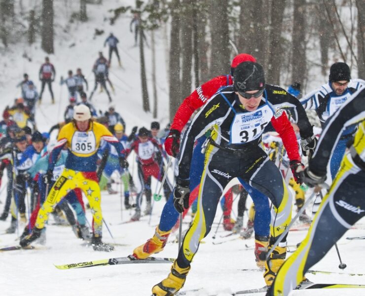 Sideline view of mass of Nordic skiers climbing uphill on race trail