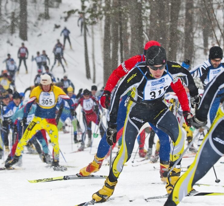 Sideline view of mass of Nordic skiers climbing uphill on race trail
